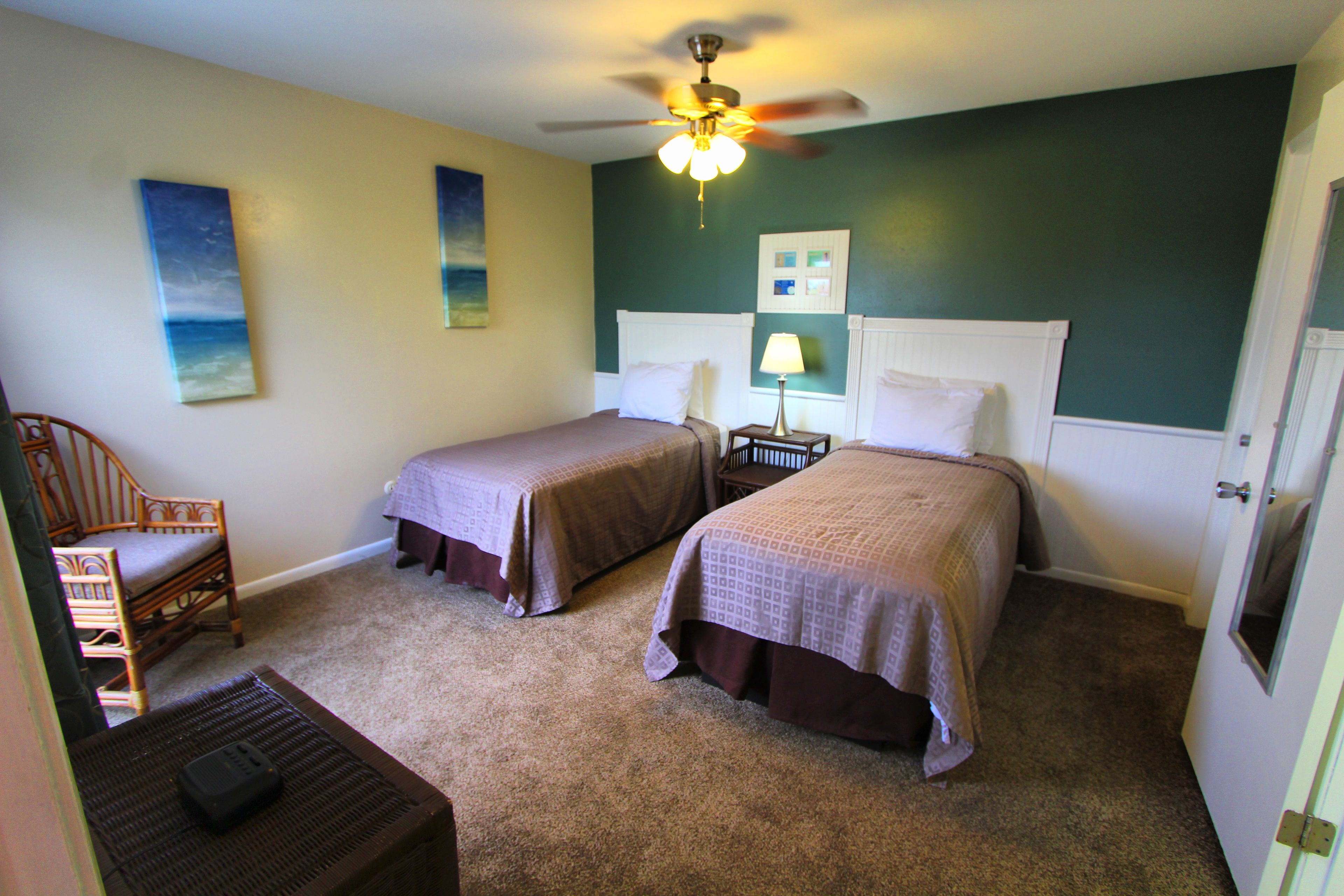 A bedroom with two beds, a ceiling fan, and a nightstand with a lamp.