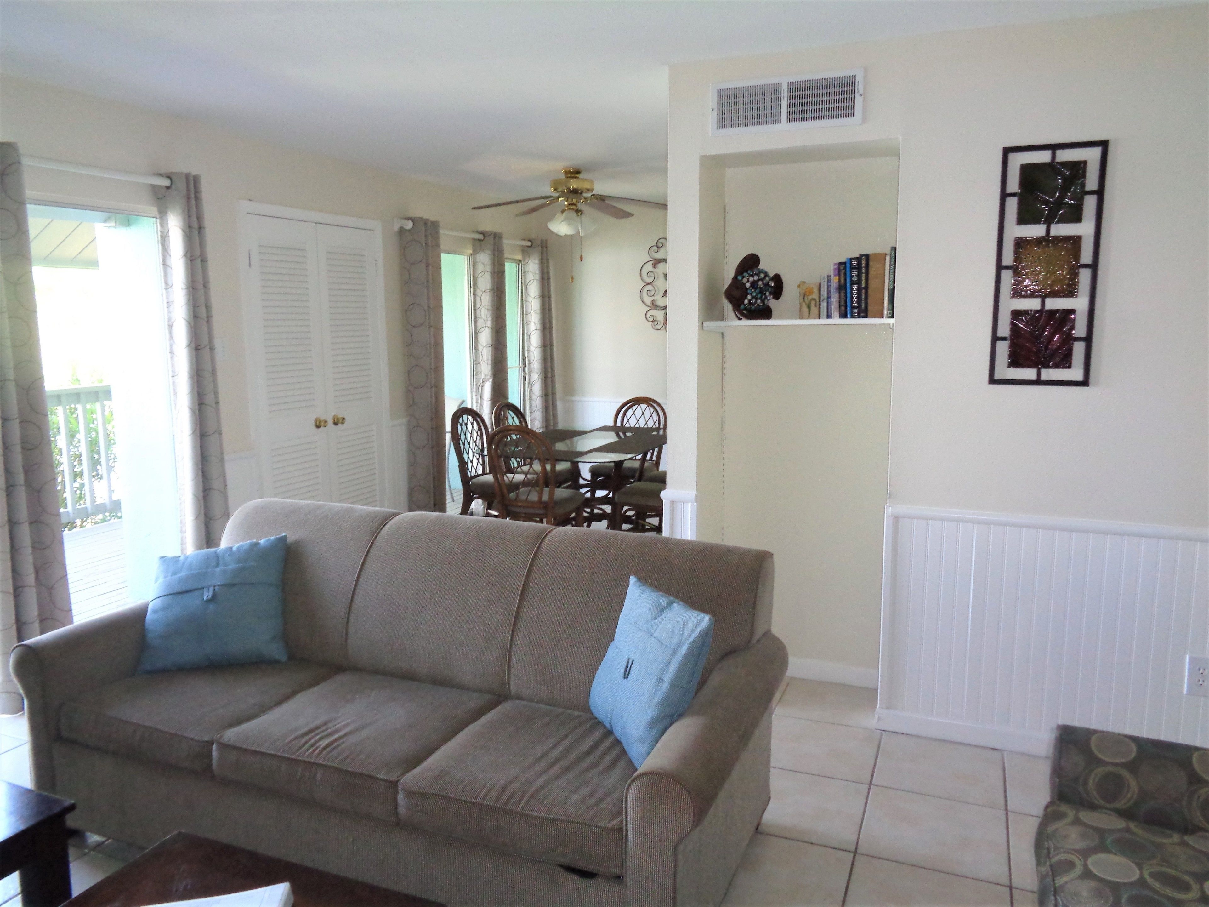 A living room with a beige sofa, two blue pillows, a wooden coffee table, and a dining area with a table and chairs.