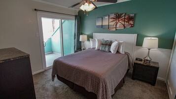 A bedroom with a bed, a ceiling fan, a nightstand, a lamp, and a view of the outside.