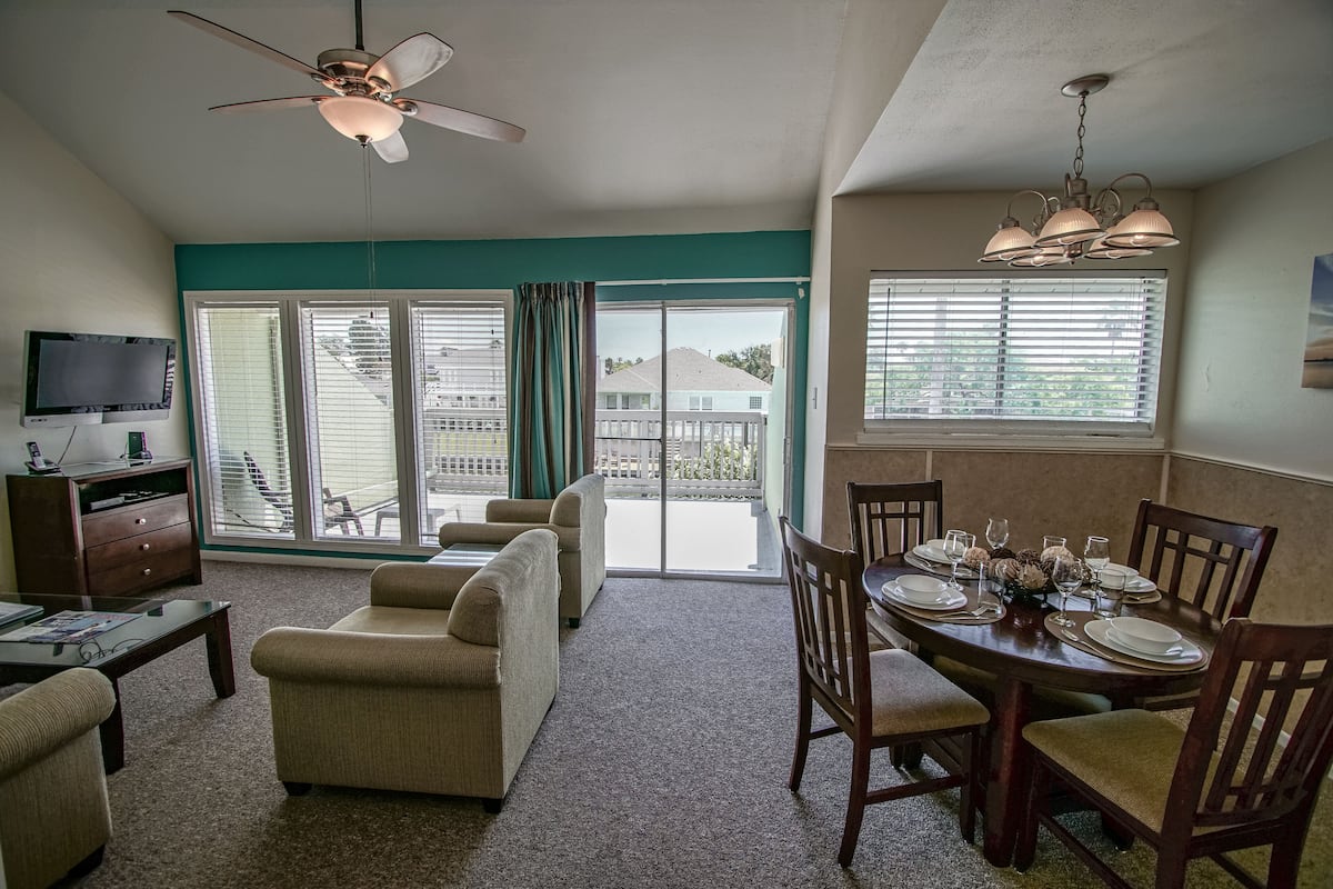 A living room with a television, sofa, and dining table set for six.