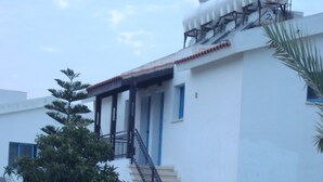 A white building with a staircase, satellite dishes, and a garden. - Socrates Apartments (Neo Chorio)