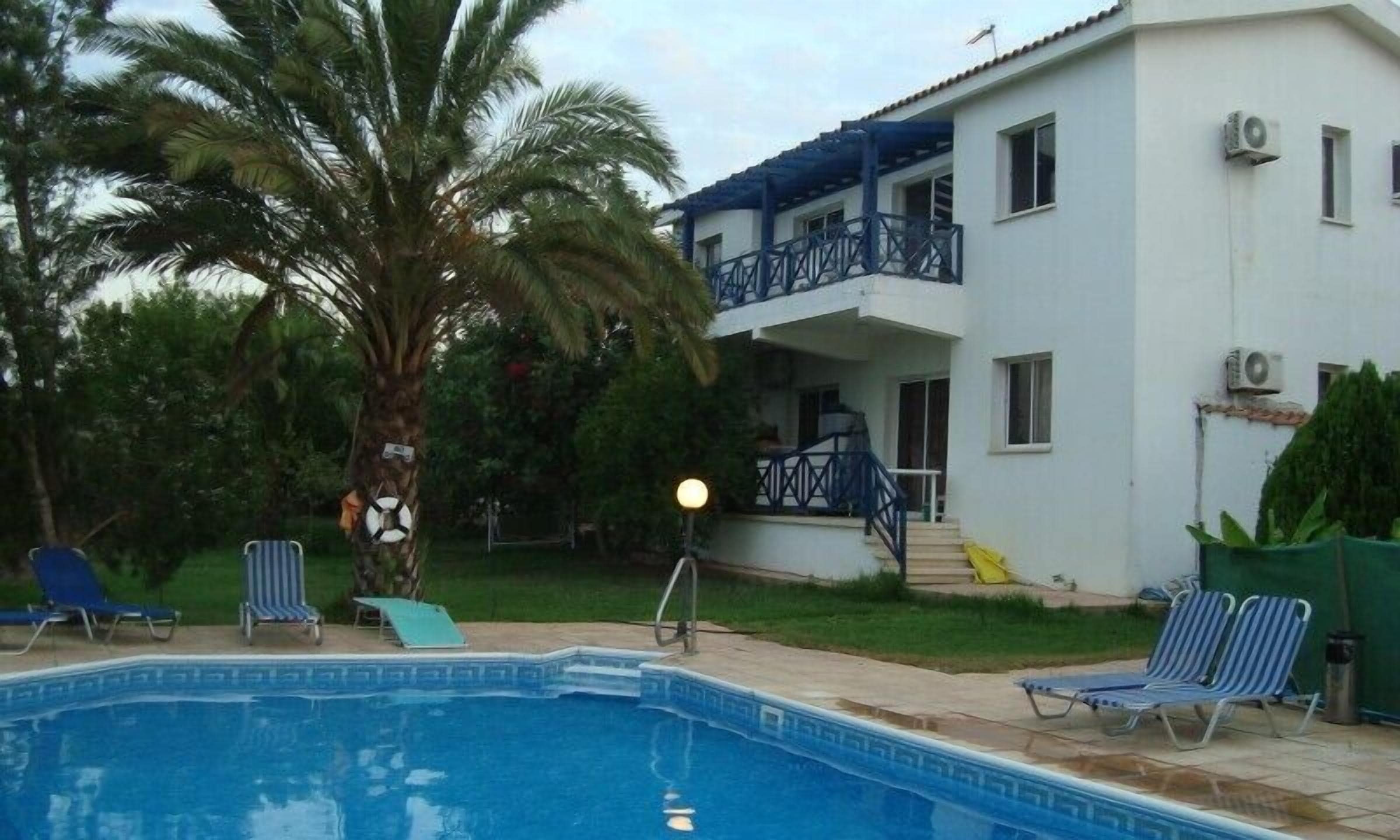 A two-story building with a swimming pool, a palm tree, and a balcony.
