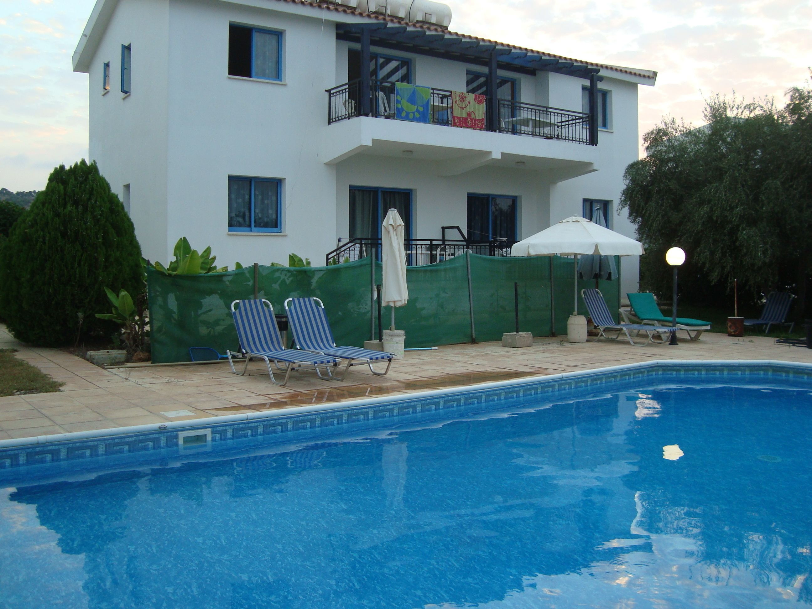 Un edificio de dos pisos con piscina, zona de estar al aire libre y valla verde.