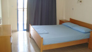 A bedroom with a wooden bed, a nightstand, a dresser, and a window with curtains. - Socrates Apartments (Neo Chorio)