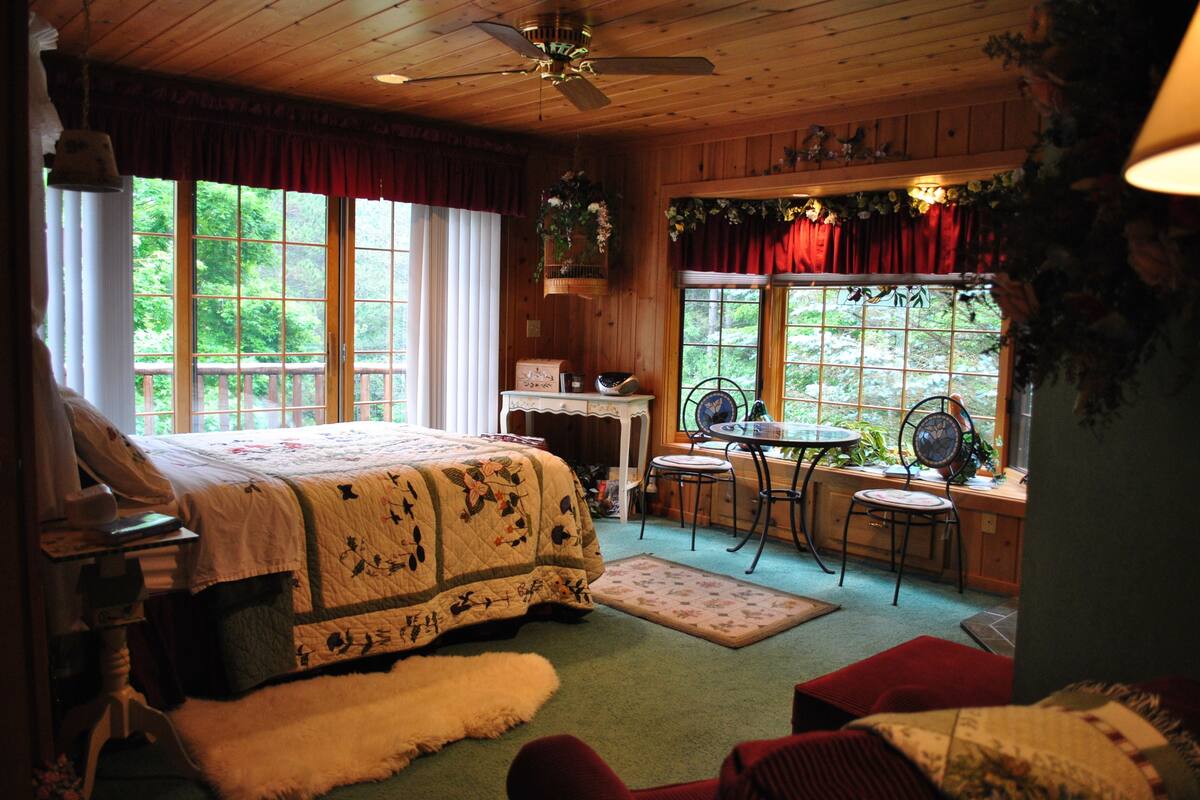 A cozy bedroom with a large bed, a desk, and a window with a view of greenery.
