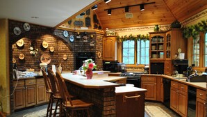 A kitchen with a brick fireplace, wooden cabinets, and a large island with bar stools. - Horton Creek Inn B&B (Charlevoix)