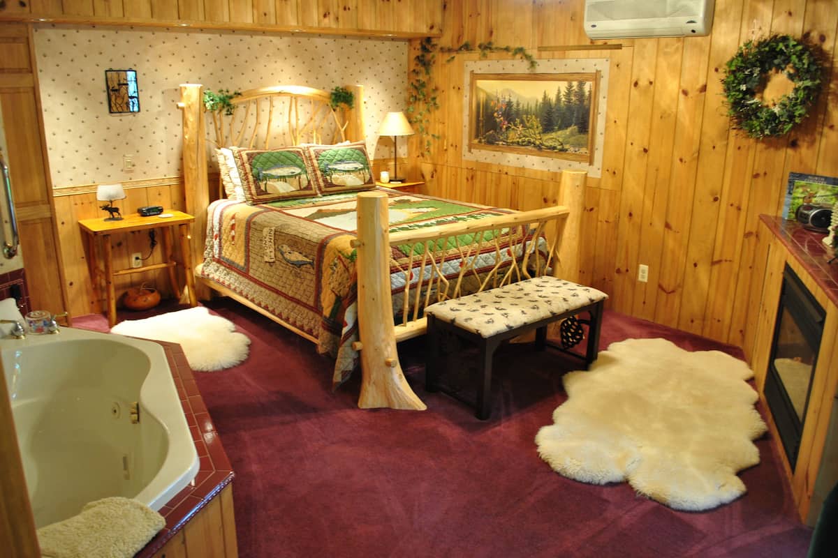 A rustic wooden room with a large bed, a wooden bench, a bathtub, and a painting on the wall.