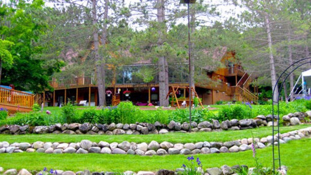 A cabin with a deck, surrounded by a landscaped garden with a stone border and various plants. - Horton Creek Inn B&B (Charlevoix)