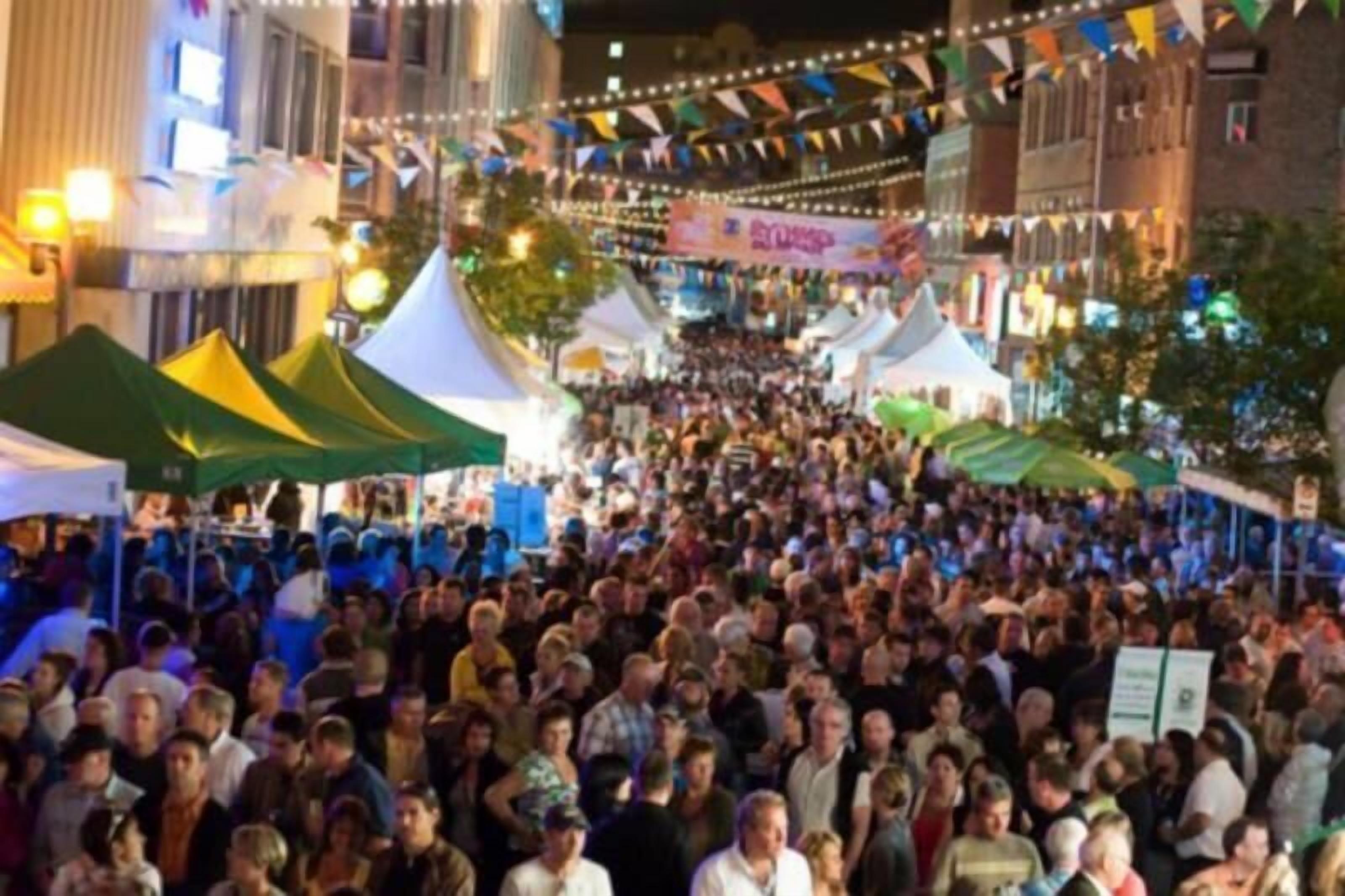 Un evento al aire libre concurrido, con carpas y banderines, probablemente una fiesta o mercado.