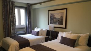 Una habitación de hotel con dos camas, una mesita de noche con lámpara, un cuadro en la pared y una ventana con cortinas.
