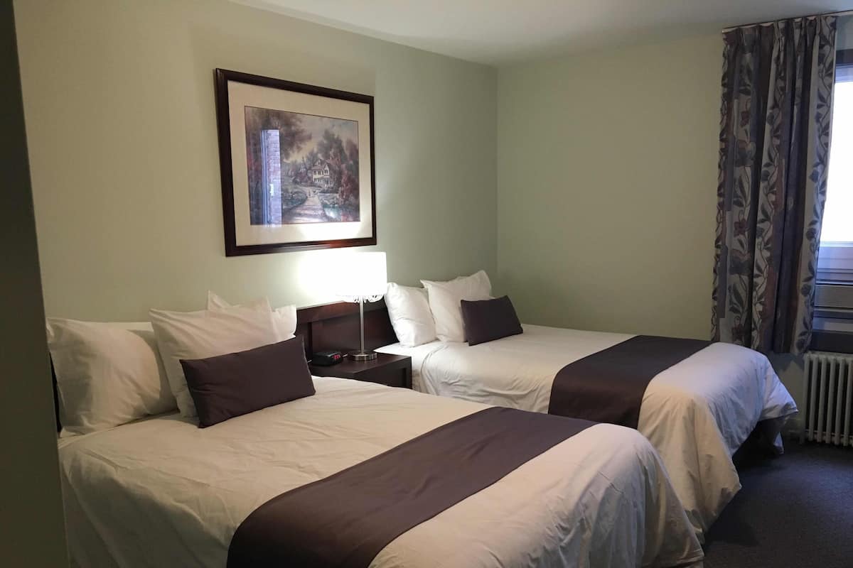 A hotel room with two beds, a nightstand with a lamp, a framed picture on the wall, and a window with curtains.