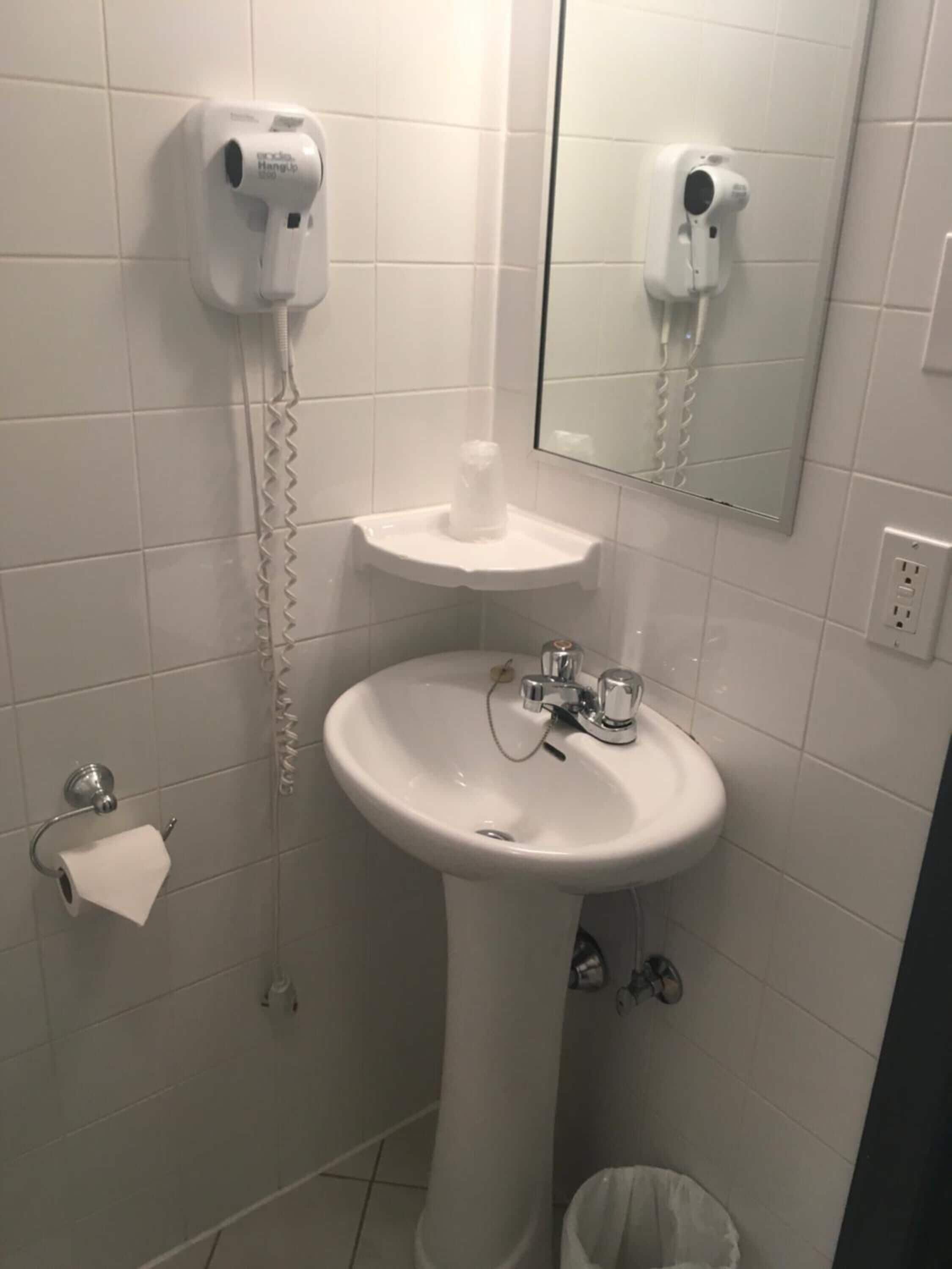 Une salle de bain avec un lavabo blanc, un miroir, un sèche-cheveux et un porte-rouleau de papier toilette.