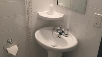 Une salle de bain avec un lavabo blanc, un miroir, un sèche-cheveux et un porte-rouleau de papier toilette.