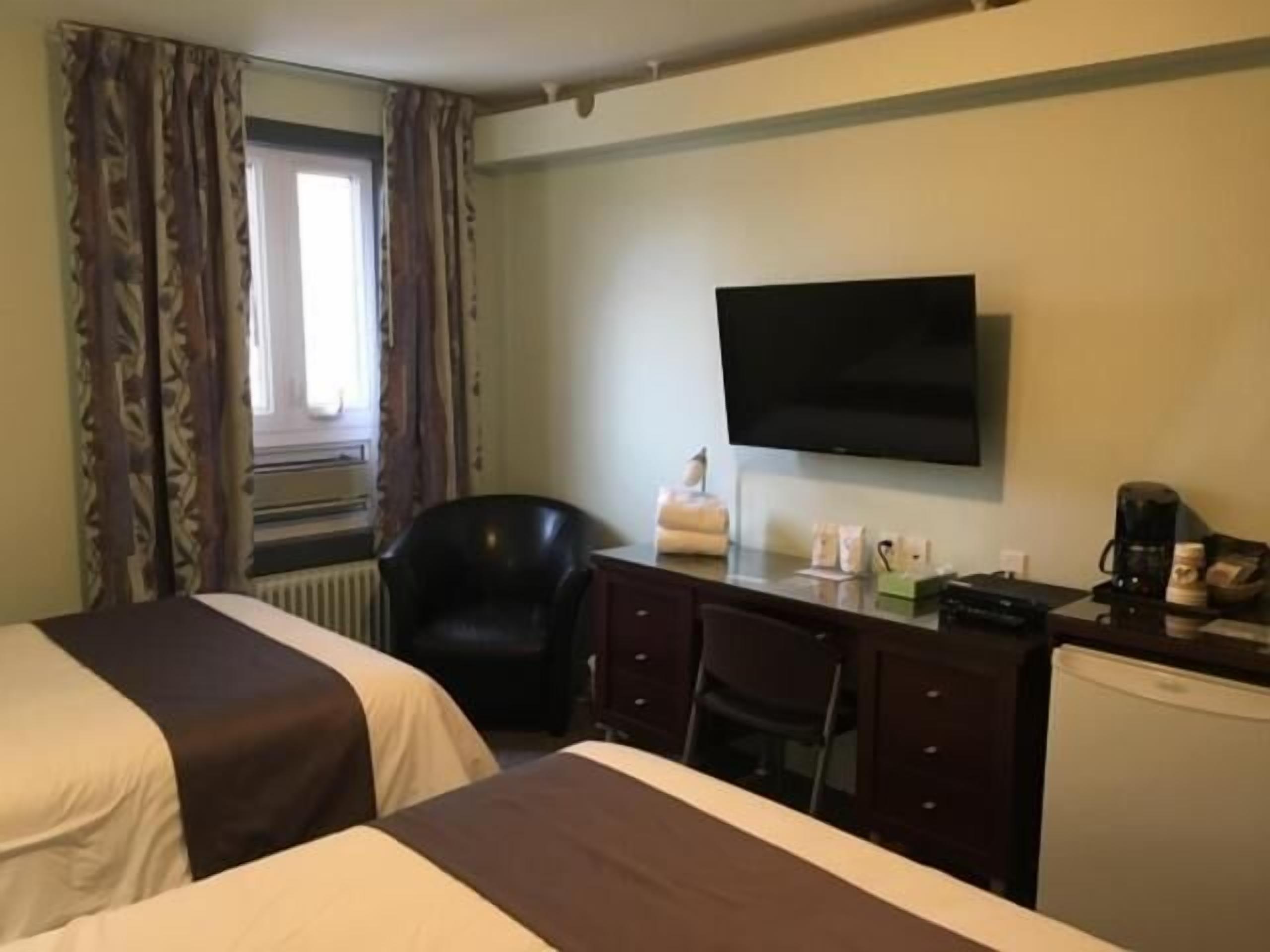 A hotel room with two beds, a desk with a flat-screen TV, a chair, and a coffee maker.