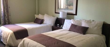 A hotel room with two single beds, each with a white and brown bedspread, a nightstand with a lamp, and a framed picture on the wall.