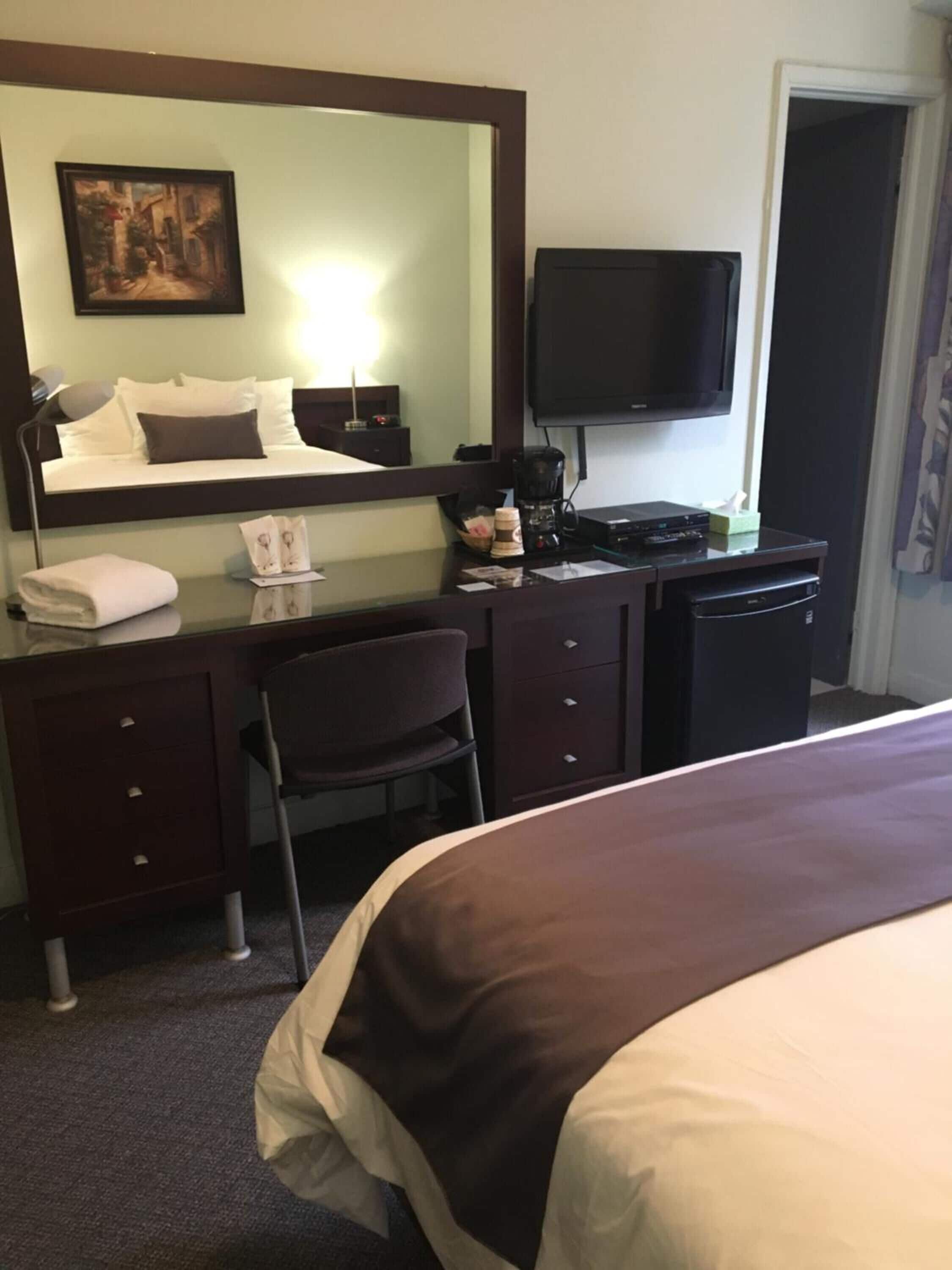 A hotel room with a bed, a desk with a chair, a television, and a coffee maker.