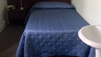 Una habitación de hotel con una cama, una mesita de noche con lámpara, un reloj de pared y un pequeño cuadro.