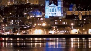 Un paisaje urbano nocturno con dos torres gemelas iluminadas reflejándose en el agua.