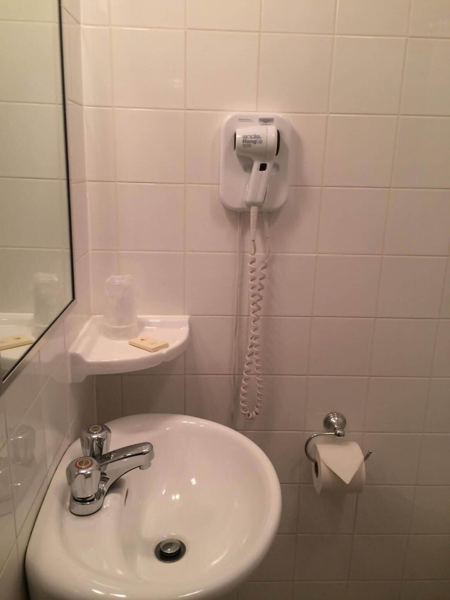 Un bagno con un lavandino bianco, uno specchio, un portasciugamani e un telefono fissato al muro.