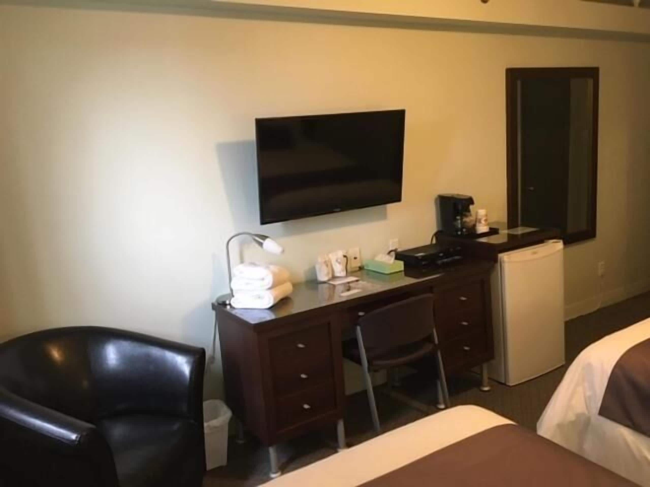 A hotel room with a bed, a desk with a chair, a television, a coffee machine, and a small refrigerator.