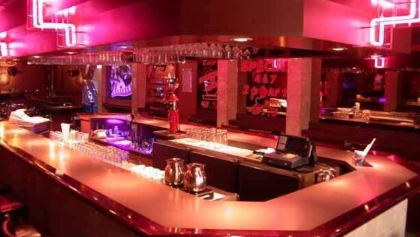 Zona de bar con mostrador, taburetes y un letrero de neón.