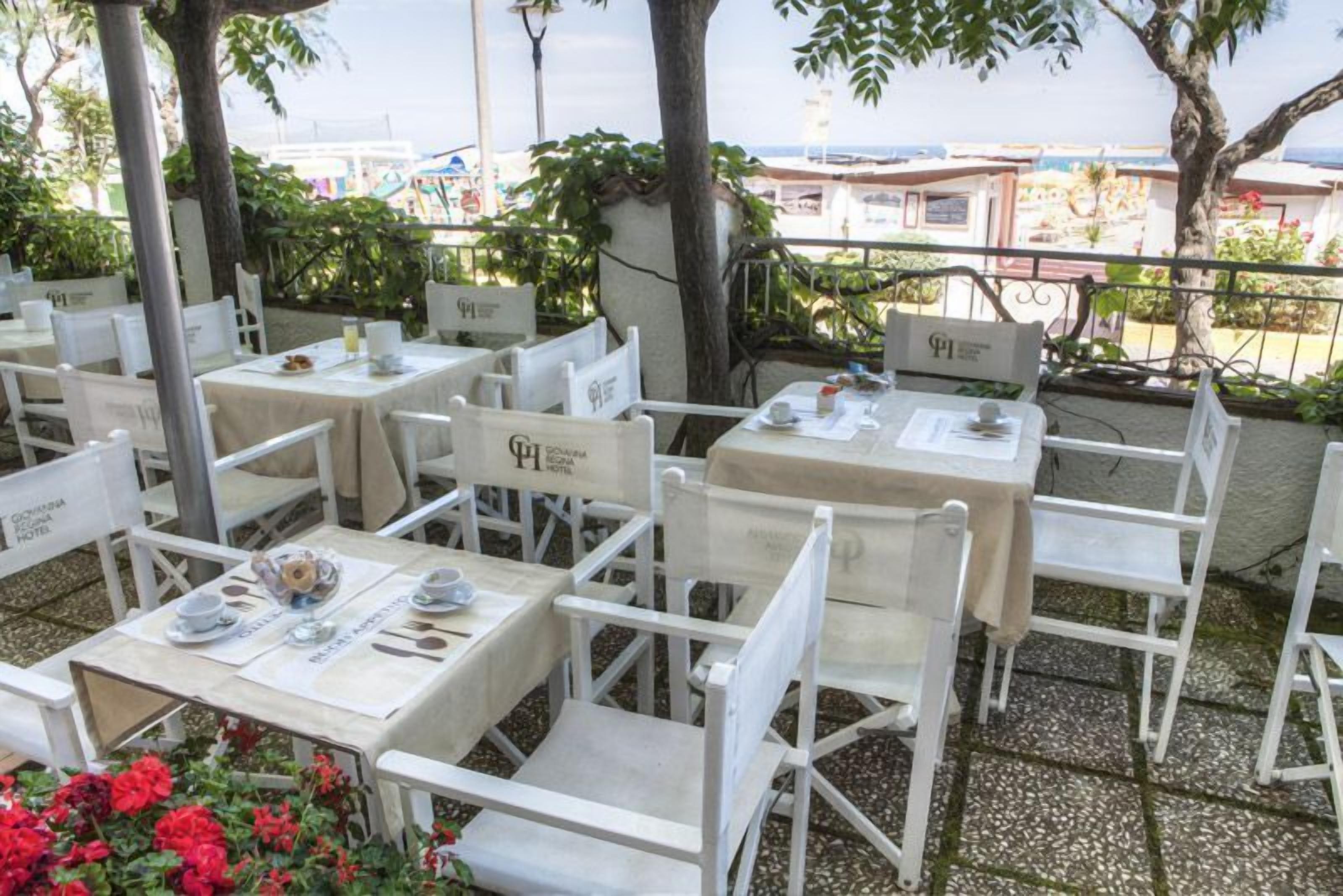 An outdoor seating area with white tables and chairs, some with signs indicating hotel names.