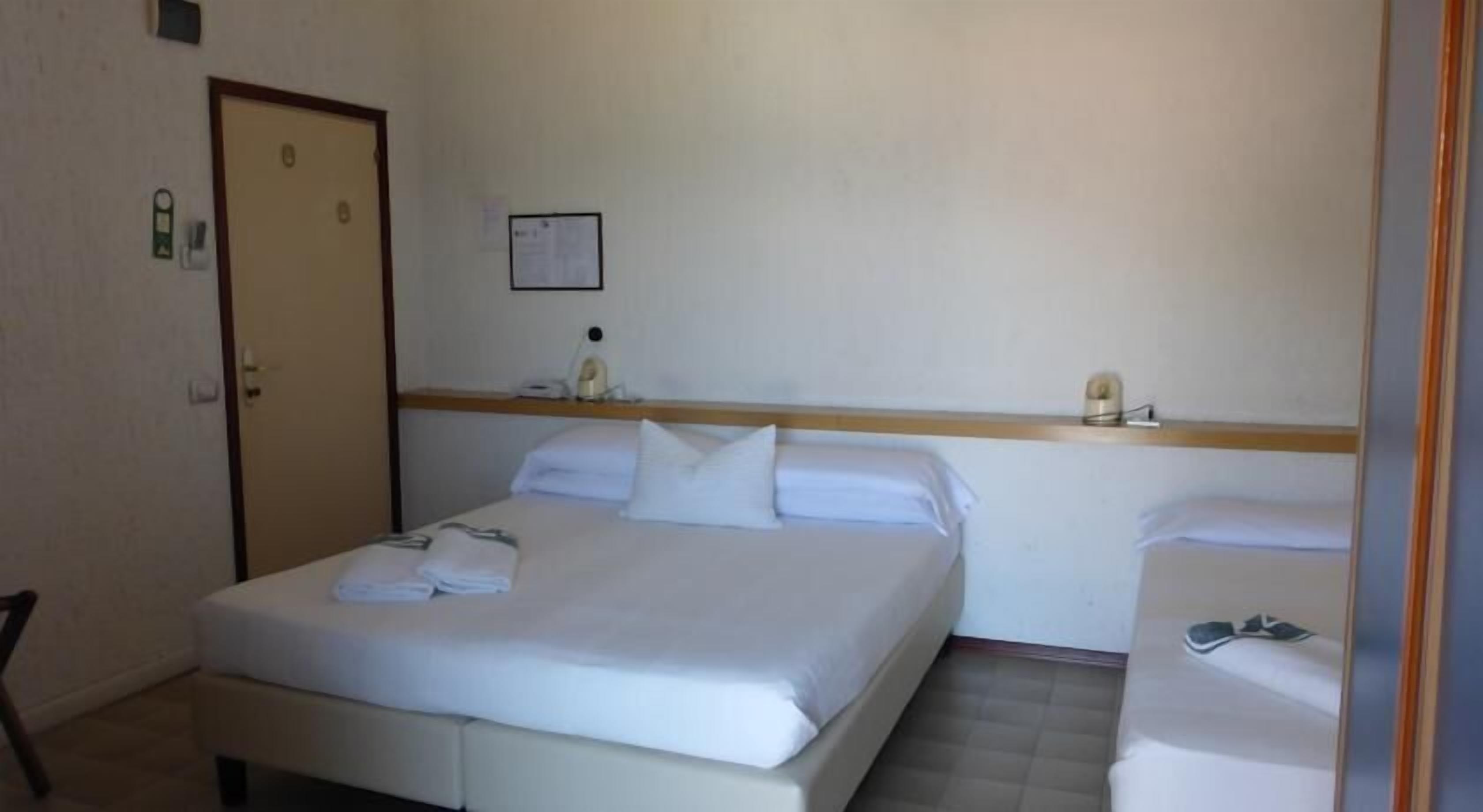 A hotel room with a bed, a bedside table, a chair, and a door.