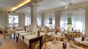 Un restaurant doté de plusieurs tables rondes, chacune recouverte d’une nappe blanche et agrémentée d’assiettes et de verres à vin.