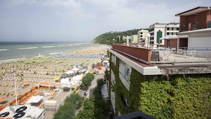Un hôtel situé sur la côte, offrant une vue sur la plage, doté de plusieurs balcons et disposant d’un espace de stationnement.