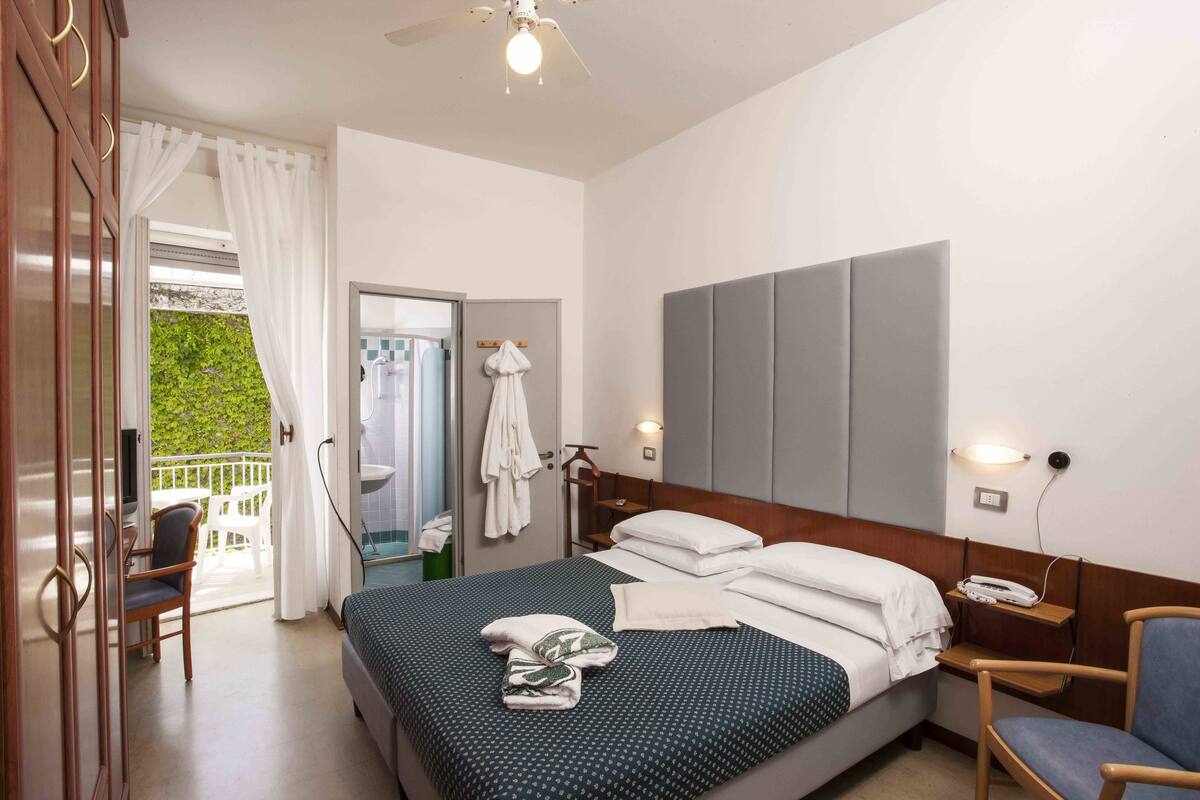 Une chambre d’hôtel avec un lit, une chaise, un bureau et un balcon donnant sur un paysage verdoyant.