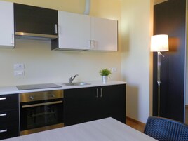 Cocina compacta con lavabo, estufa y alacenas. Hay una pequeña planta en maceta sobre la encimera y una lámpara de pie junto al lavabo.