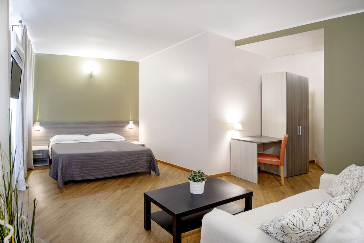 A modern hotel room with a bed, desk, chair, and a small table with a plant.