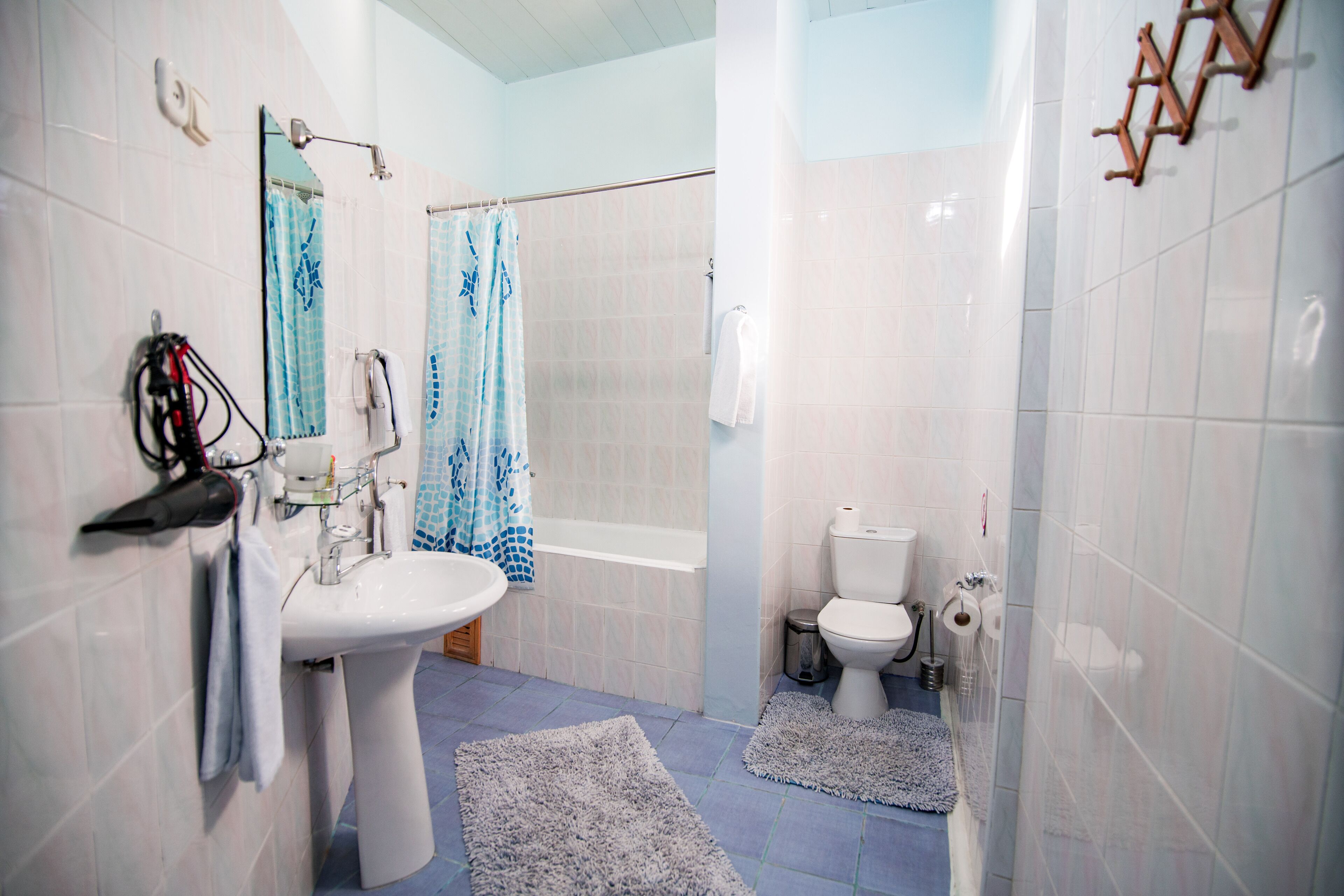A bathroom with a sink, toilet, and bathtub. There are towels hanging on the wall and rugs on the floor.