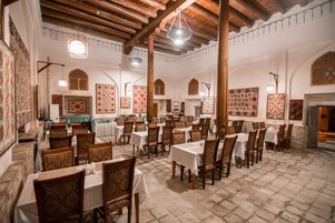 Un comedor amplio con múltiples mesas y sillas, techos altos de madera y diseños decorativos en las paredes.