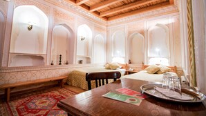 Une chambre traditionnelle avec un plafond en bois, un lit avec une tête de lit, un banc, une table avec un plateau et un tapis à motifs.