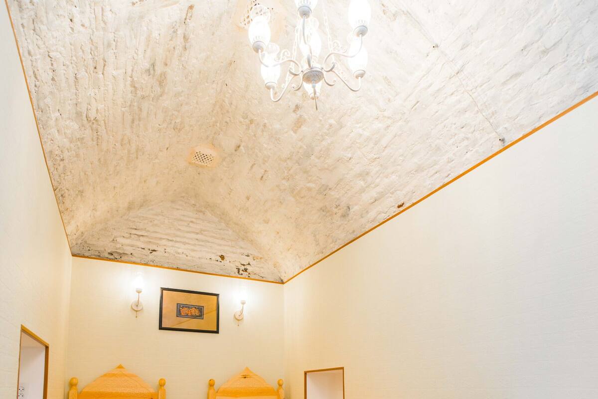 Ein Zimmer mit zwei Holzbetten, farbenfroher Bettwäsche, einem weißen Stuhl, einem Tisch und einer Kronleuchter.