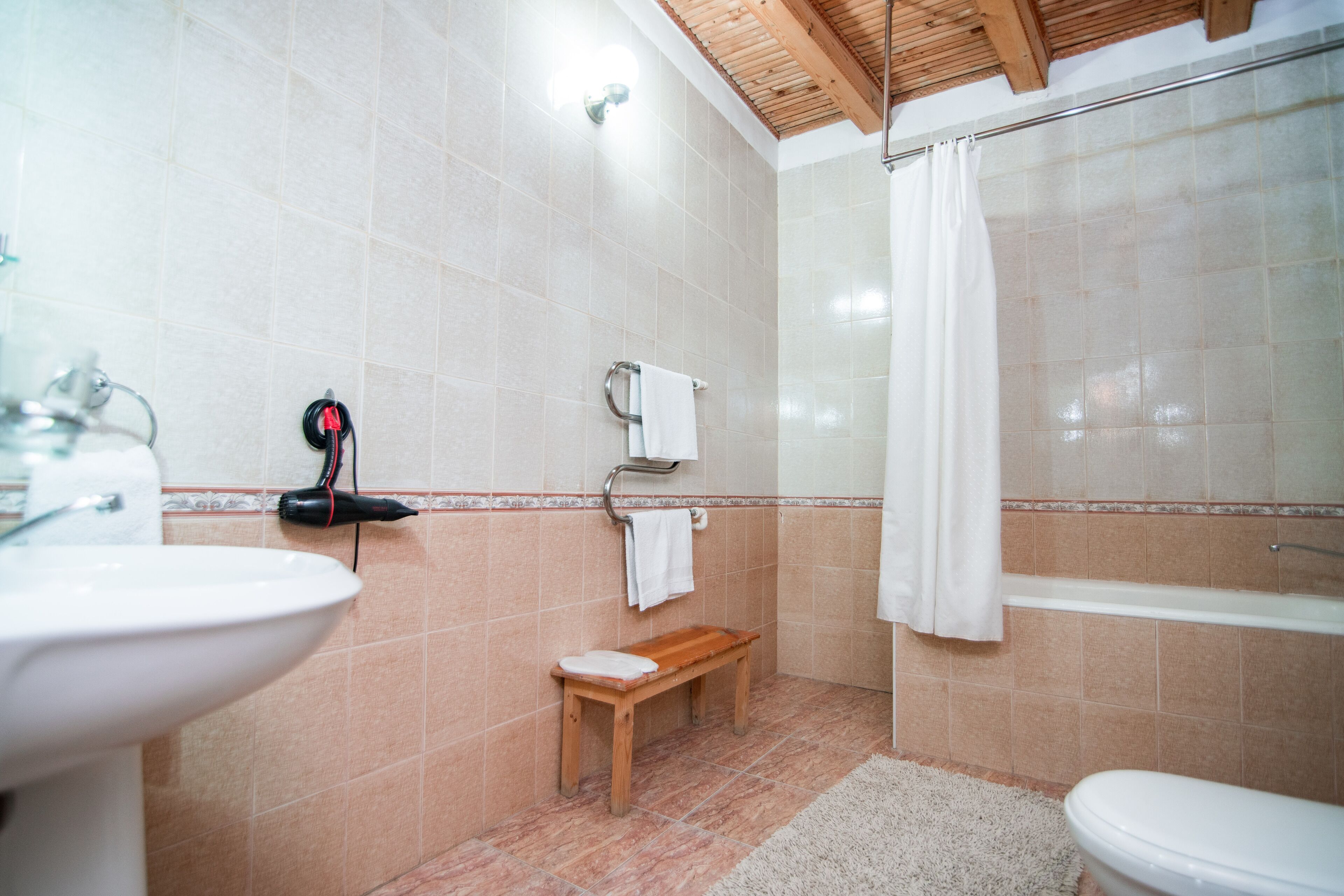 A bathroom with a sink, toilet, shower, and a small wooden bench.