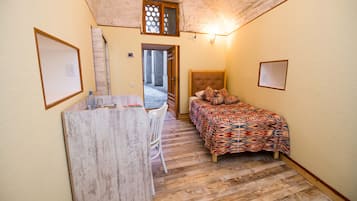 Una habitación pequeña y acogedora con una cama, un escritorio y una silla. Hay una ventana que da al exterior y una puerta que conduce a otra habitación.