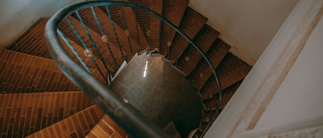A spiral staircase with a metal handrail and brick steps.