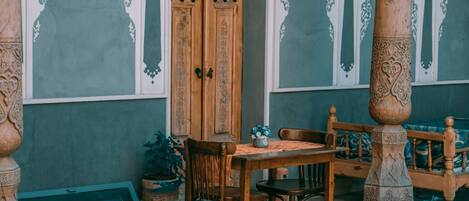 Une table en bois avec des chaises, une plante en pot et un banc en bois dans une pièce aux murs à motifs et dotée d’une porte en bois.