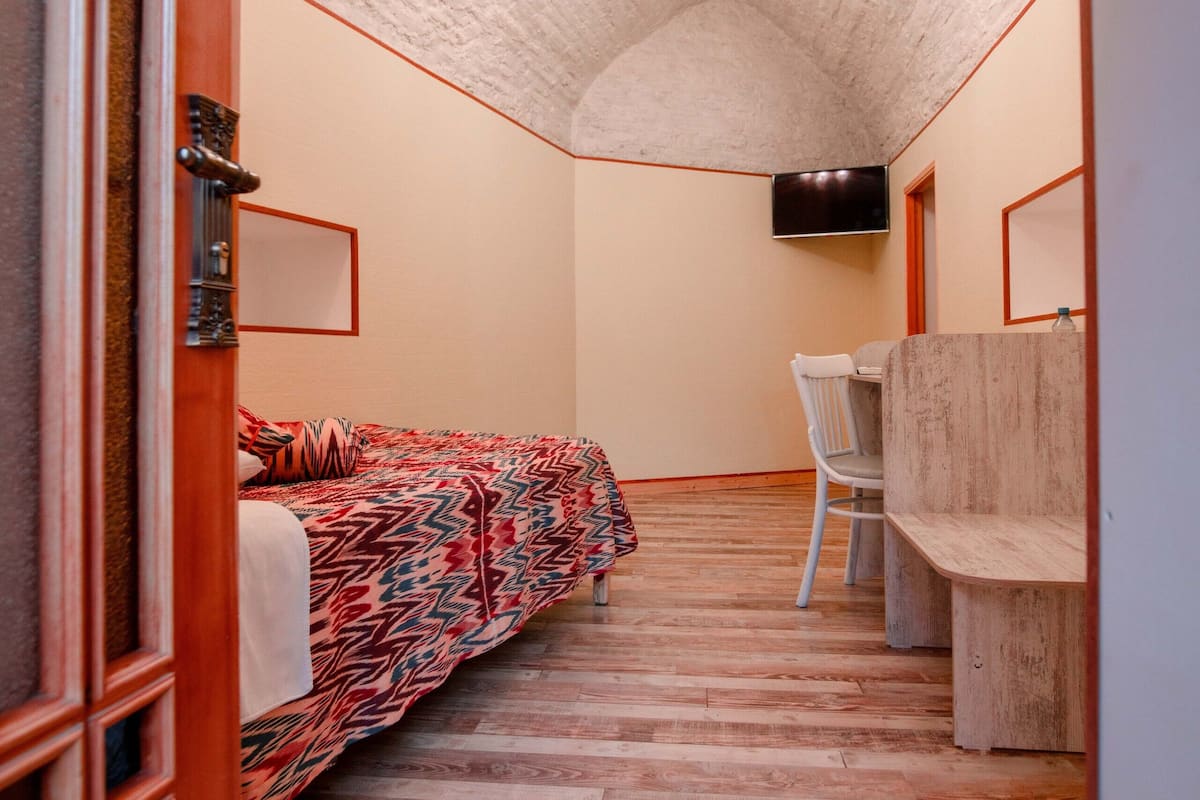 Ein schmales Dielenkorridor mit einem Bett mit gemustertem Überwurf, einer Holzbank und einer Deckenleuchte.