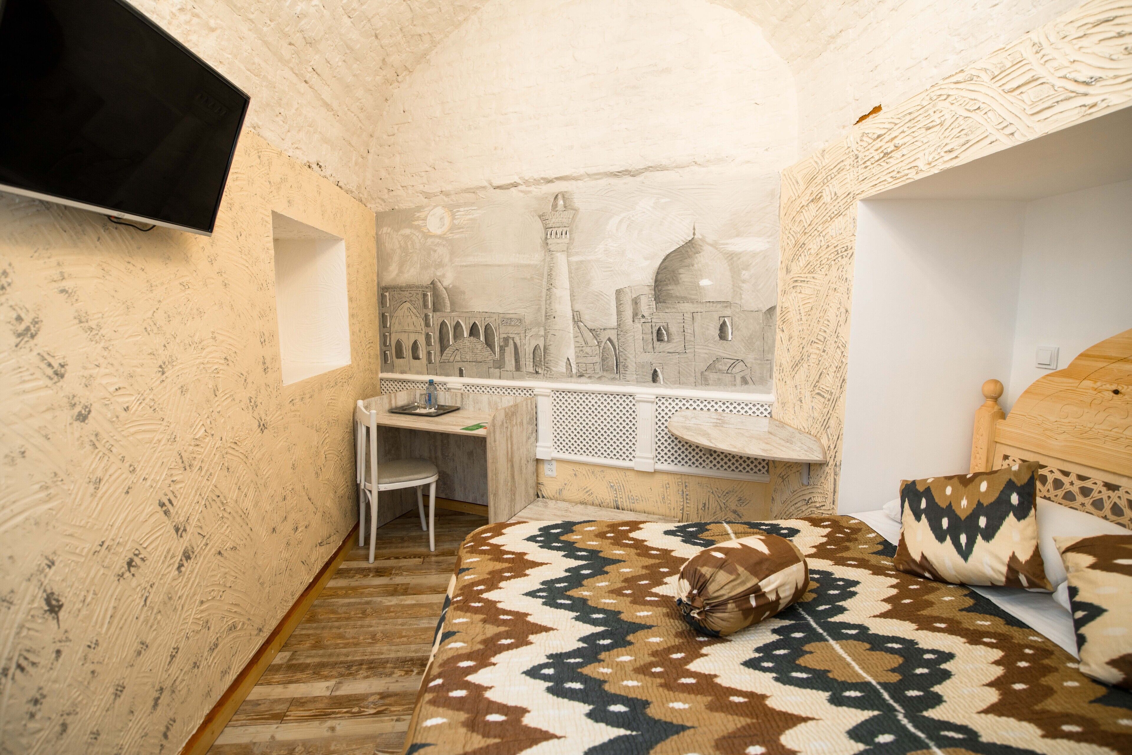 A bedroom with a patterned bedspread, a desk, and a wall mural of a mosque.