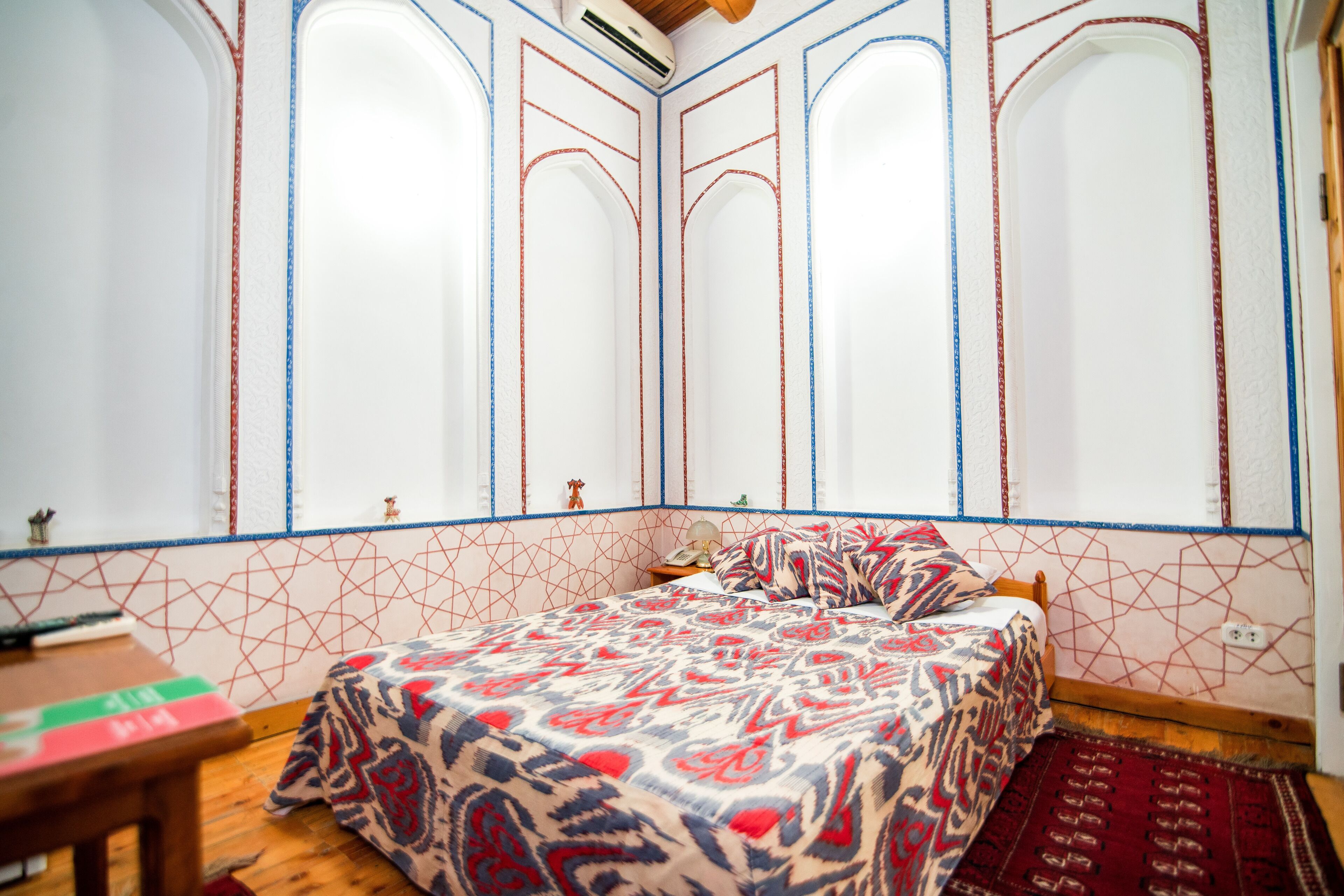 Une chambre à coucher avec une couvre-lit à motifs, une table de chevet en bois et un tapis rouge.