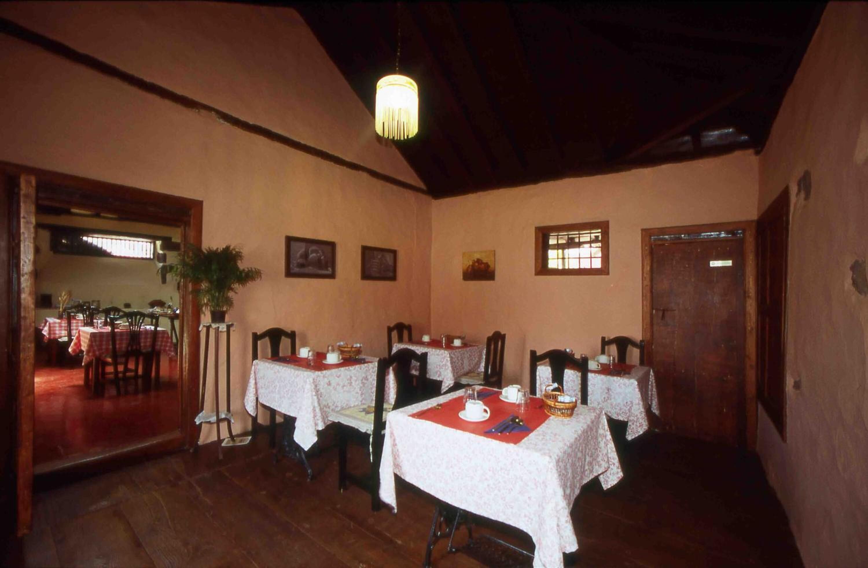 Un espace repas avec des tables et des chaises en bois, un lustre et des tableaux encadrés accrochés aux murs.