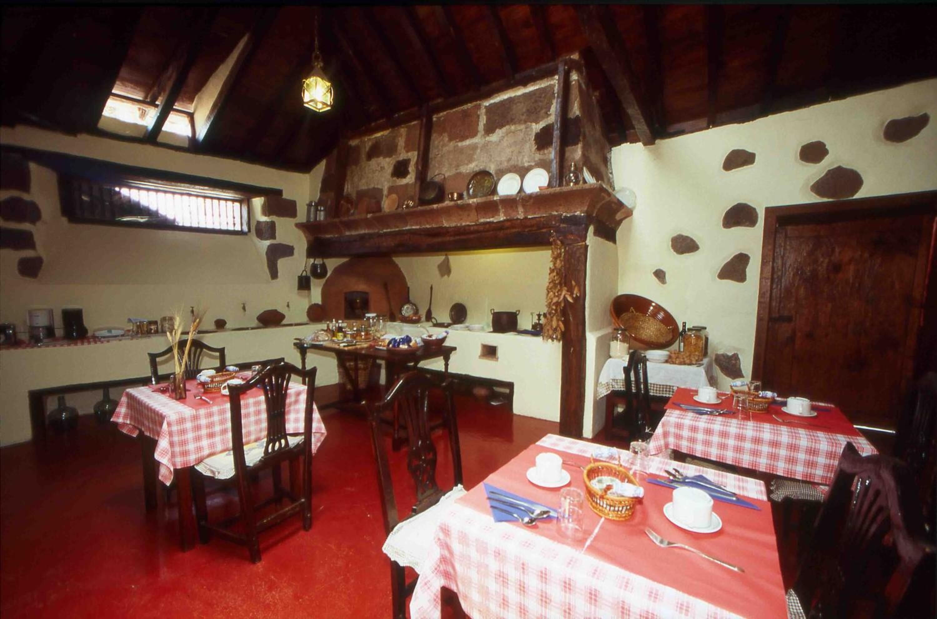 Un comedor rústico con mesas y sillas de madera, paredes de piedra y un alto techo de madera.