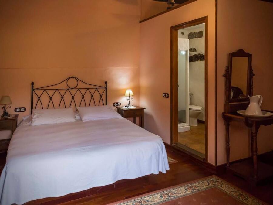 A bedroom with a bed, bedside table, lamp, and a mirror.
