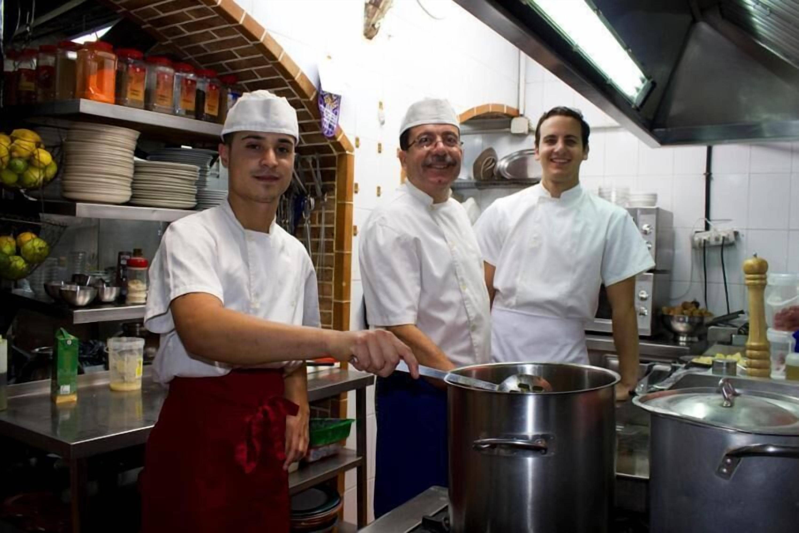 Una cocina profesional con cocineros, equipo de cocina de acero inoxidable y estantes llenos de ingredientes.