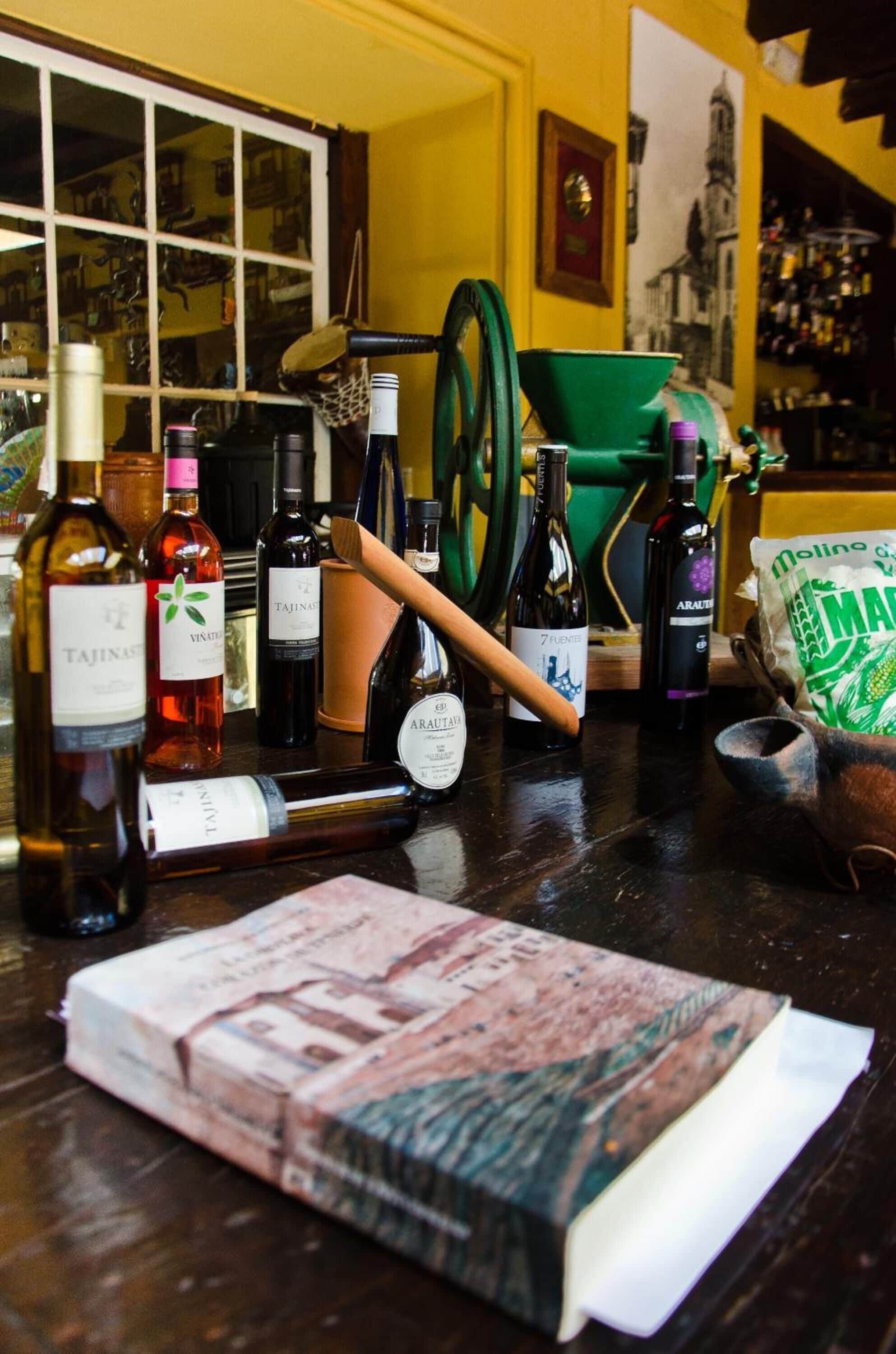 Una barra con varias botellas de alcohol, un embudo verde y un libro.
