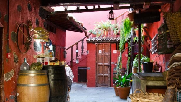 Une ruelle étroite ornée de barils en bois, de plantes en pot et d’une décoration rustique.