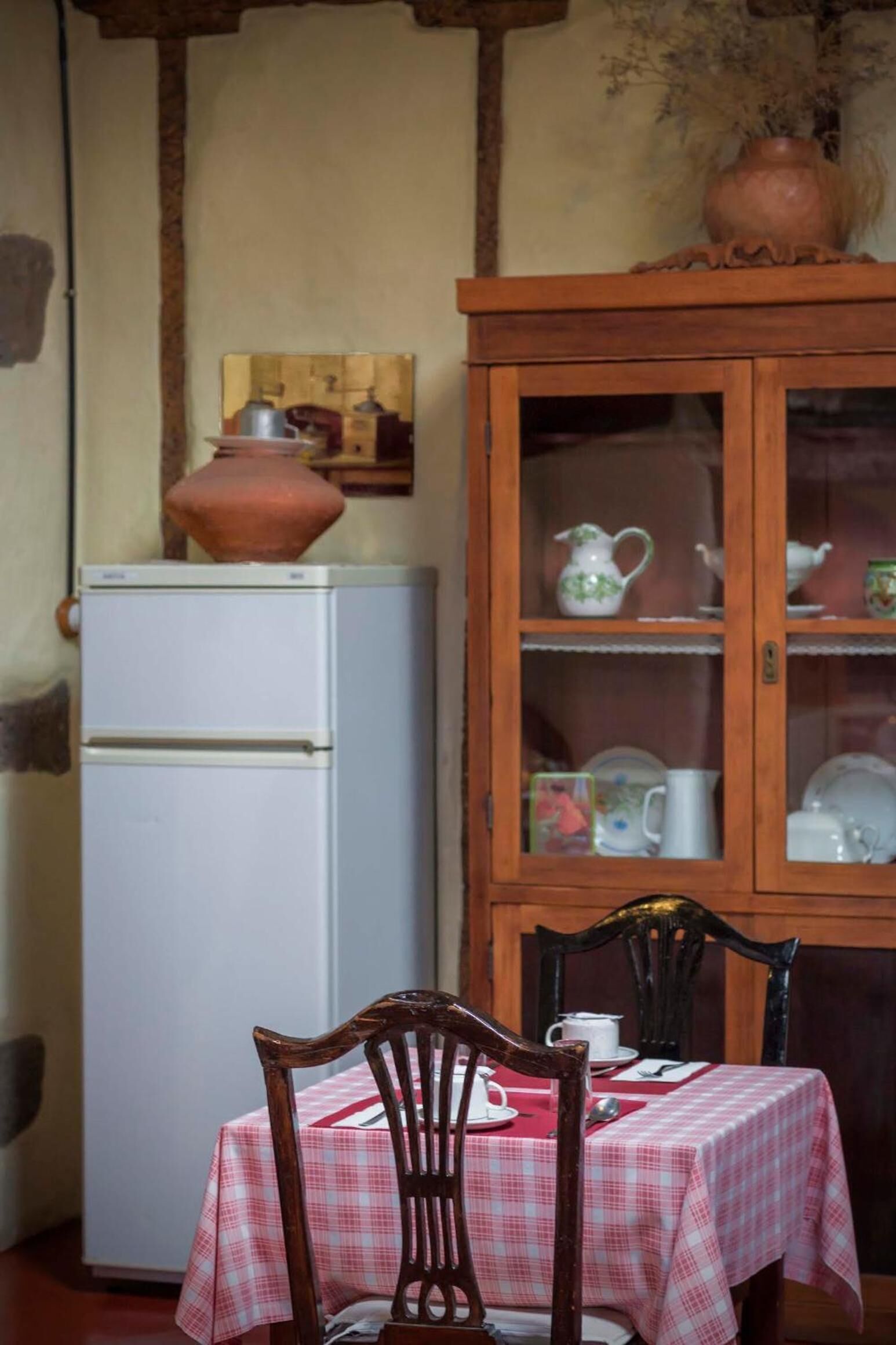 Un comedor con una mesa preparada para dos, un armario con puertas de vidrio y un refrigerador blanco.